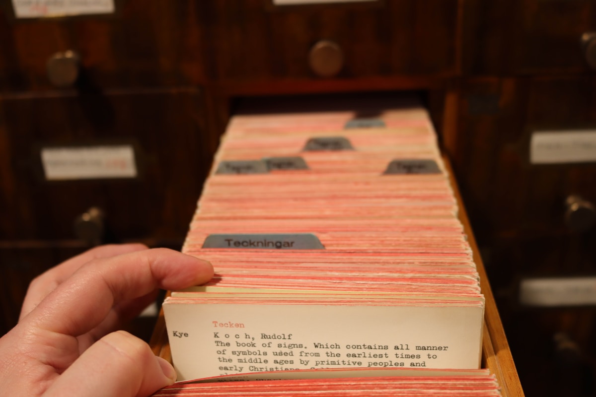A hand pulling a card from a wooden library card catalog drawer, with rows of indexed cards